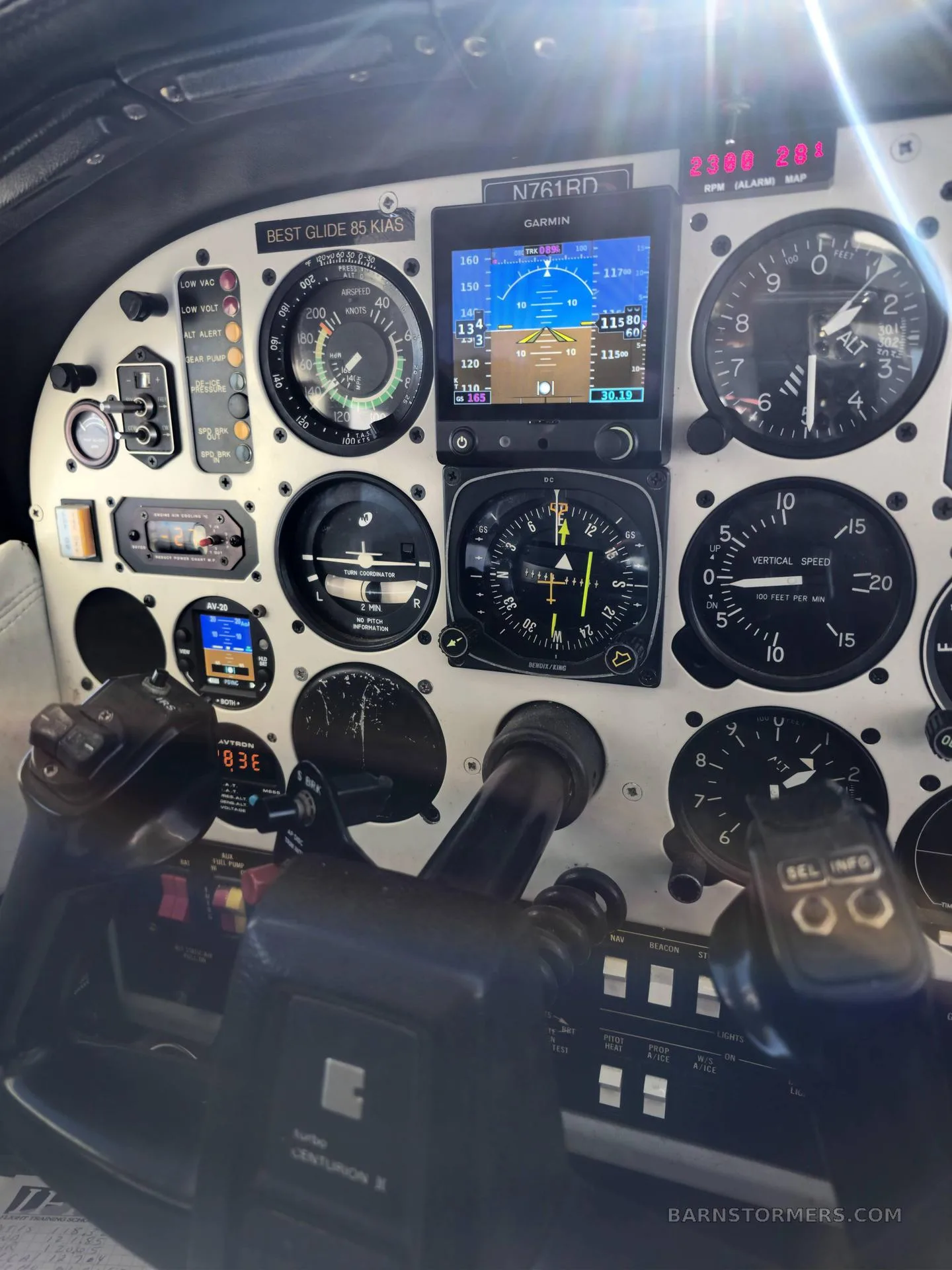 A close-up view of a small aircraft's instrument panel, featuring analog gauges and a Garmin navigation display.