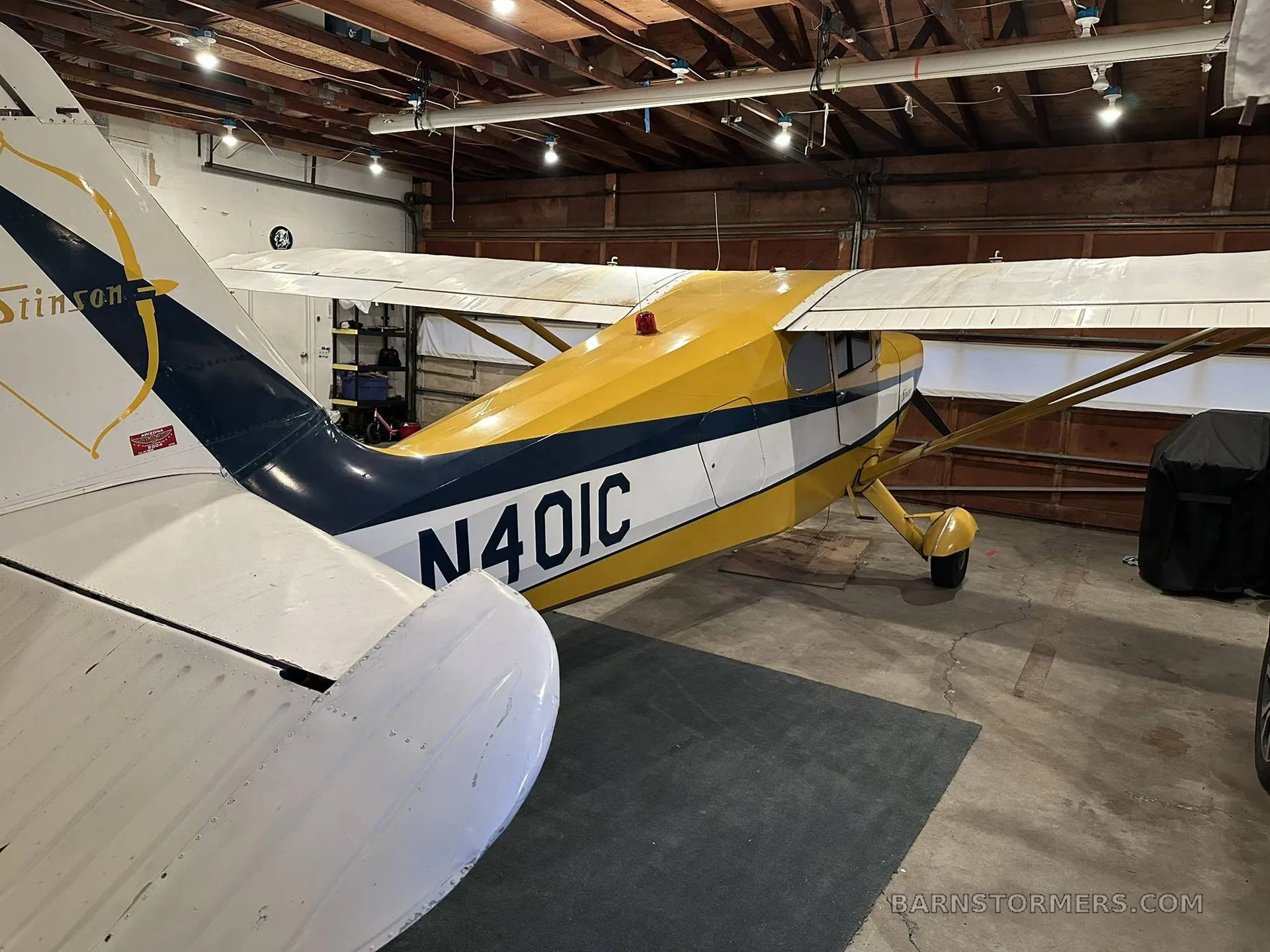A rear-side view of the yellow and blue Stinson aircraft, N401C, parked in a garage.