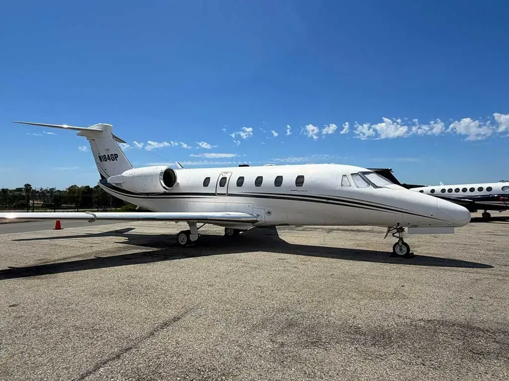 A white Cessna Citation business jet (N184GP) with a dark stripe, parked on an asphalt tarmac under a clear blue sky.