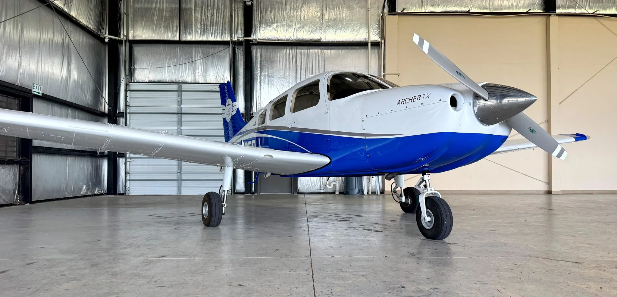 A front view of the white and blue Piper Archer TX aircraft, N105DJ, parked in a hangar.