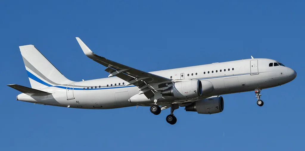 A white Airbus A320 family aircraft with blue and grey stripes on the tail and fuselage, flying with landing gear extended against a clear blue sky.