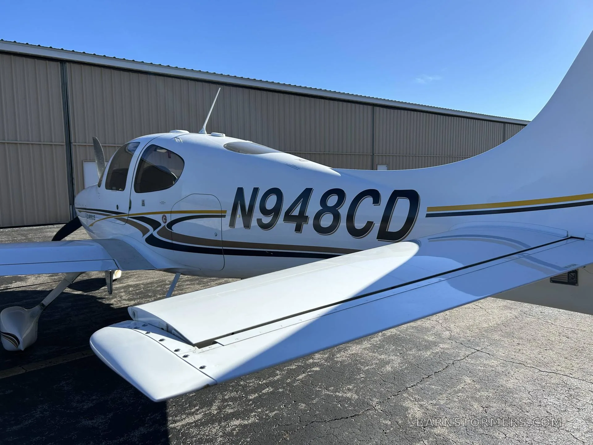 A close-up view of the tail and wing of a white Cirrus SR22 aircraft with gold and black stripes, registration N948CD.