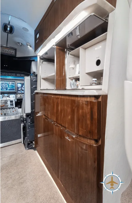 A close-up of the aircraft's galley with dark wood cabinetry and a view into the cockpit.
