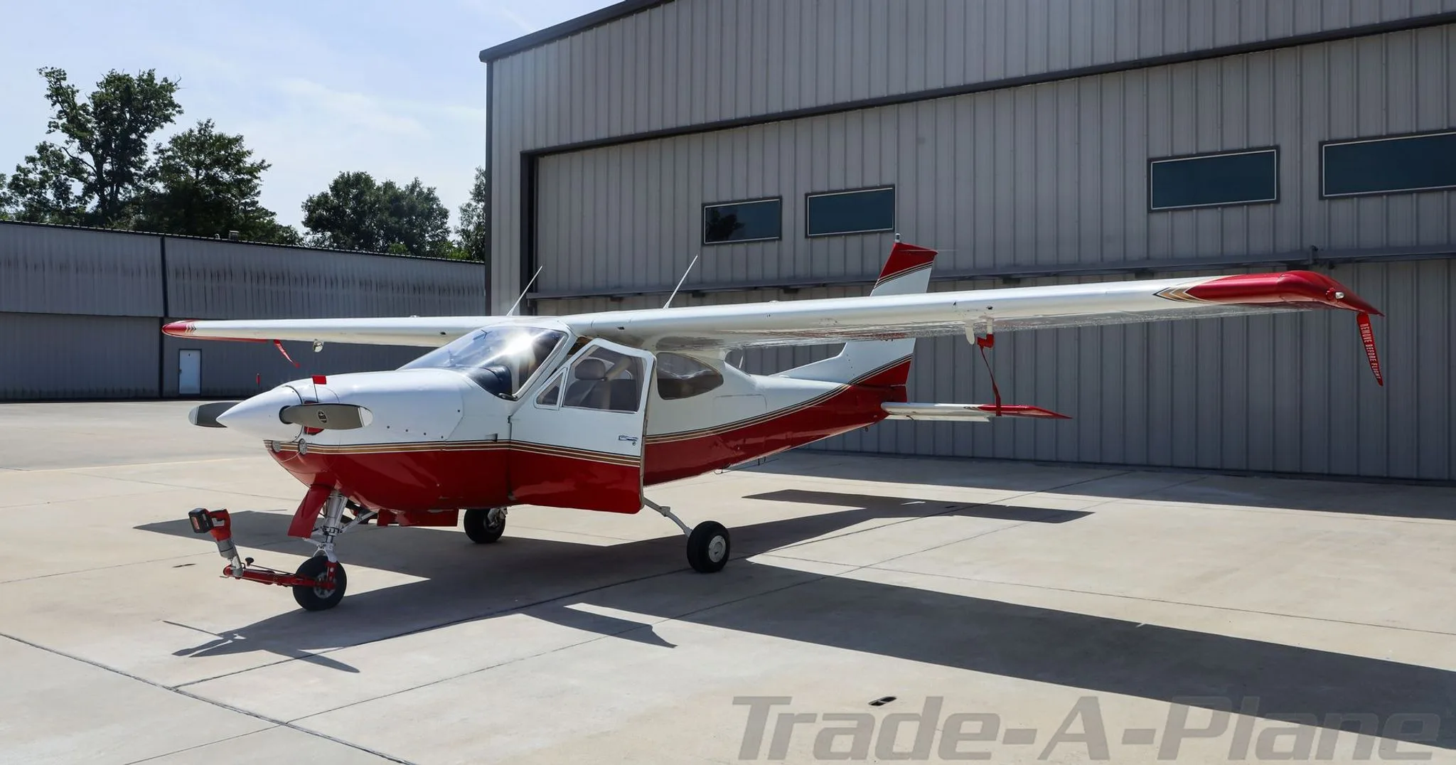A red and white Cessna 177RG Cardinal with its door open, parked on an airfield.
