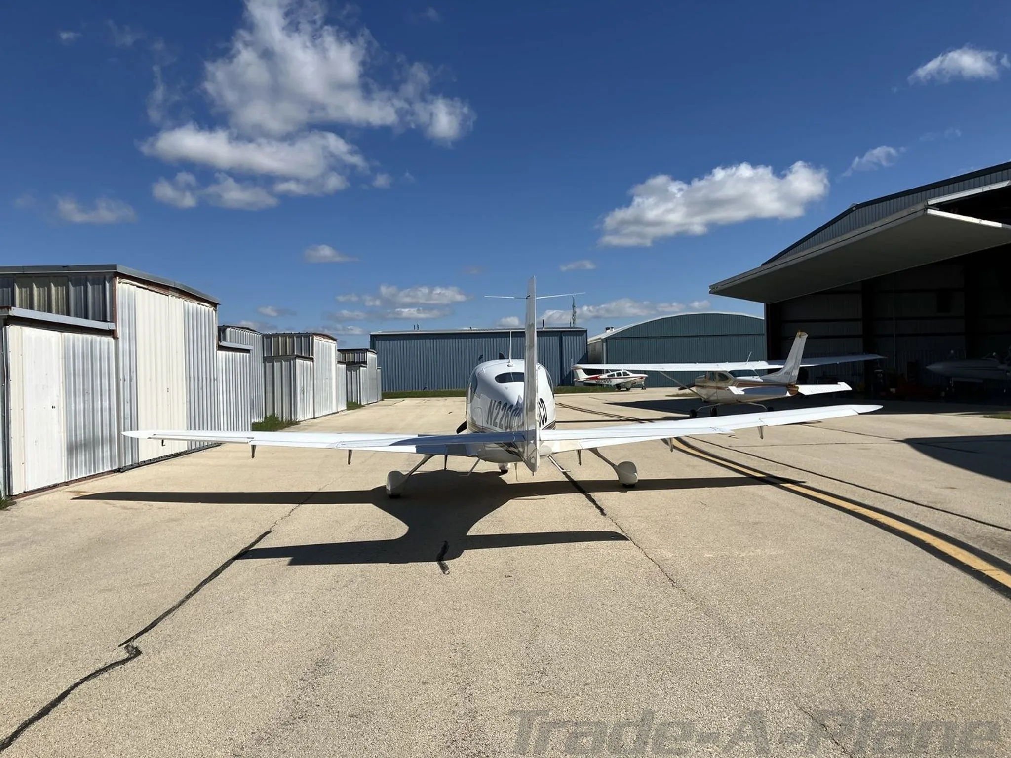 A white Cirrus SR20 aircraft, tail number N226CD, viewed from the rear on an airfield tarmac with hangars and other aircraft in the distance.