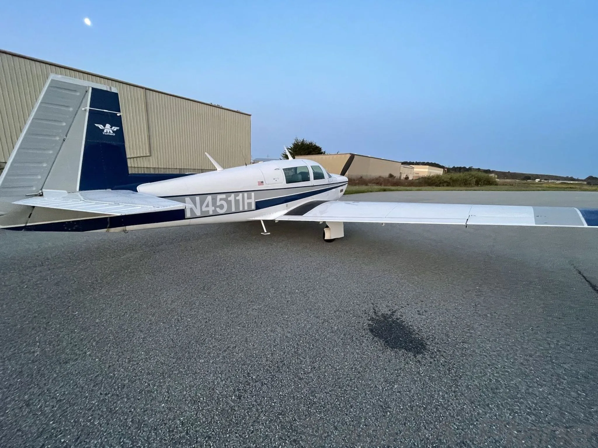 A white and blue single-engine aircraft, N4511H, viewed from the rear left on an airport ramp at dusk.