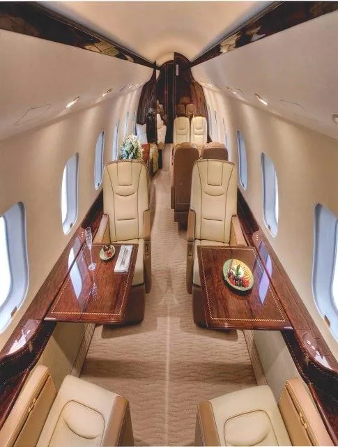 A luxurious aircraft cabin interior with beige leather seats, polished wood tables, and a floral centerpiece.