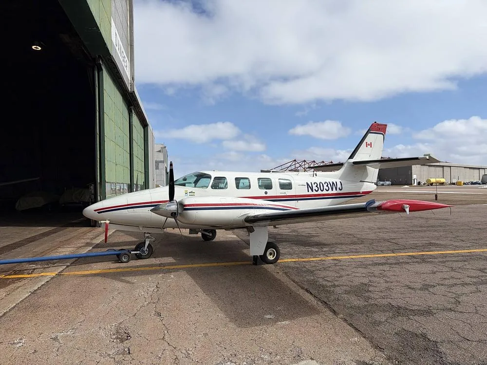 A white twin-engine aircraft with red and blue stripes, N303WJ, parked outside a hangar.
