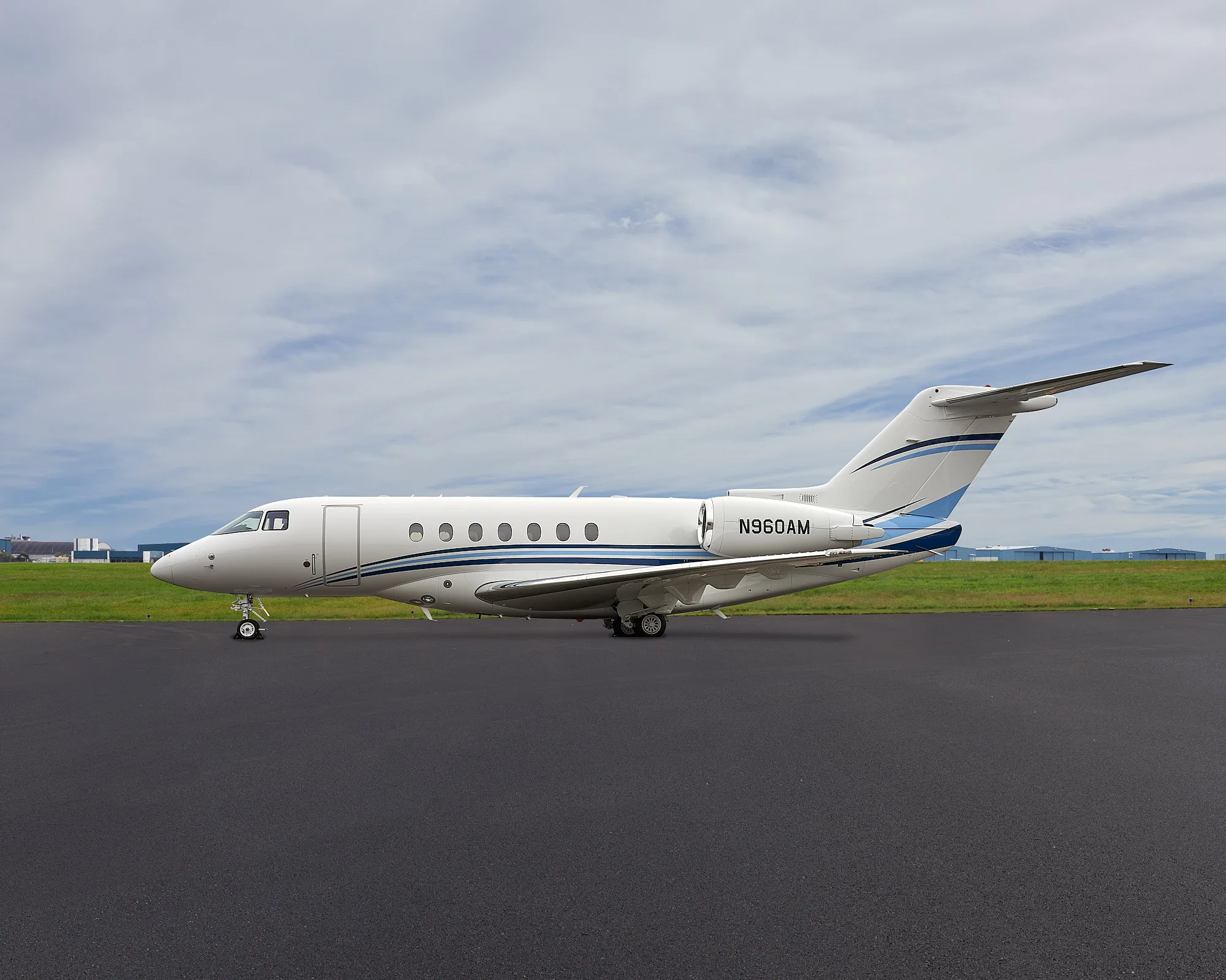 A white business jet with blue stripes, registration N960AM, parked on an airport tarmac under a cloudy sky.