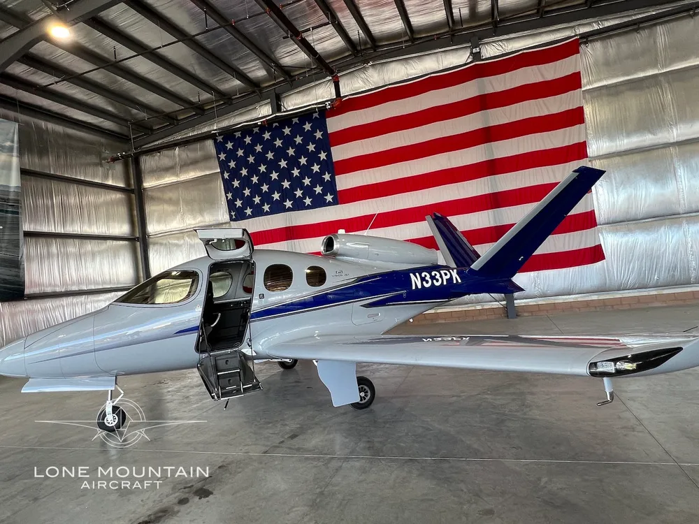 Side view of a grey and blue Cirrus Vision Jet (N33PK) with its main door open, parked in a hangar.