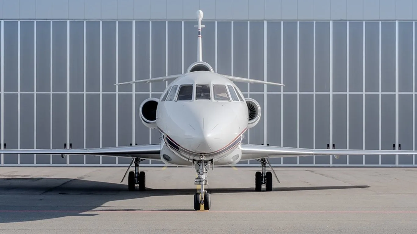 A white business jet with a red and blue stripe on the tail, parked on an tarmac in front of a modern hangar.