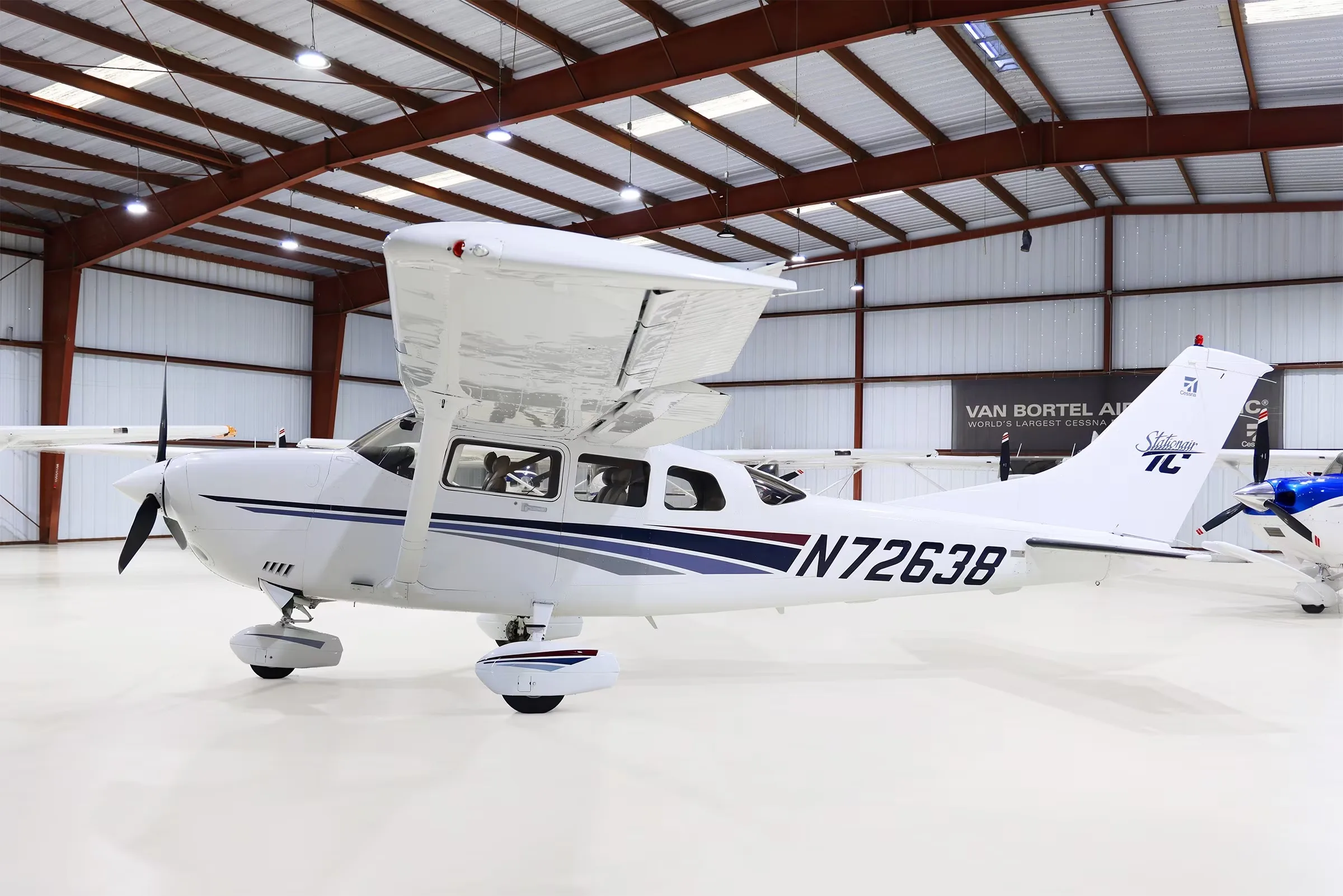 A white Cessna Stationair TC aircraft (N72638) with blue and gray stripes is parked in a hangar.