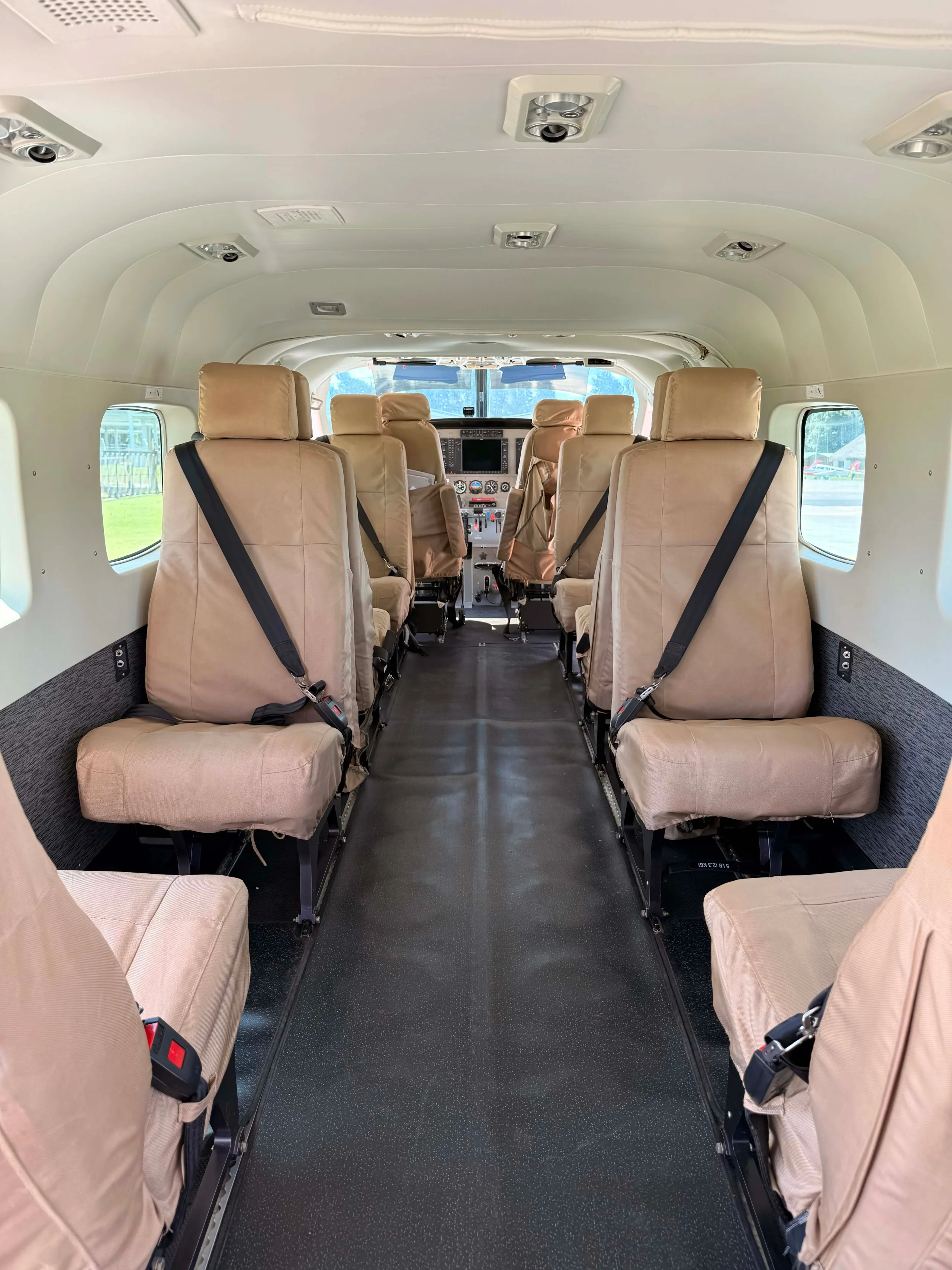 The interior cabin of an aircraft with tan fabric seats leading to the cockpit.