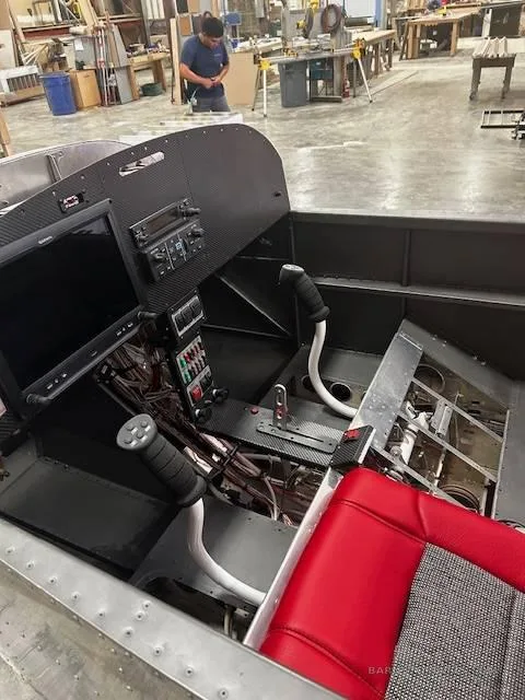 The cockpit of a partially assembled aircraft, showing the instrument panel with screens, controls, and a red seat.
