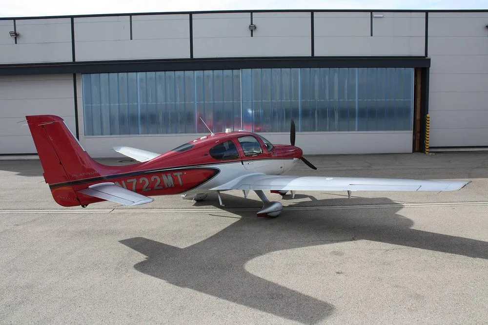 A red and white Cirrus SR22 aircraft, registration N722MT, parked on an asphalt apron, showing its right side.