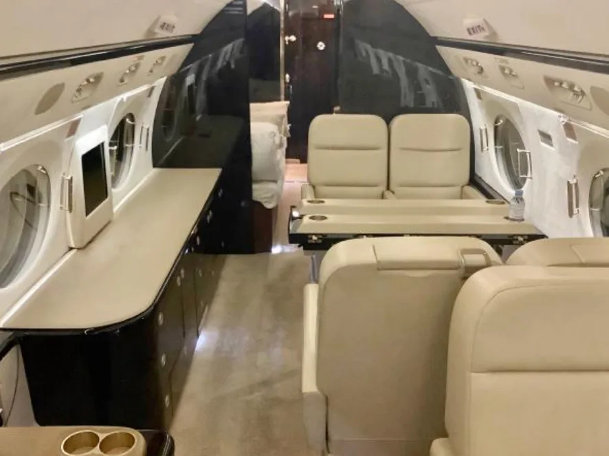 A view of the private jet's cabin, featuring cream seating, a long counter, and a bed in the rear.