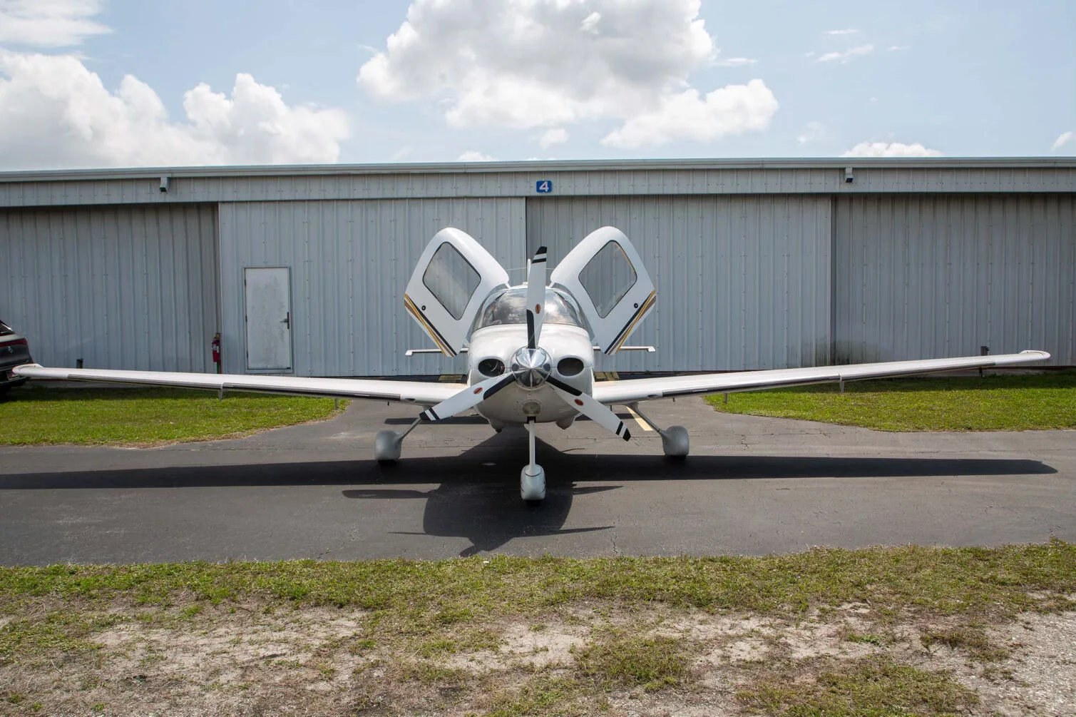 A white Cirrus SR22 aircraft, registration N806EC, with both gull-wing doors open, parked head-on in front of a hangar.