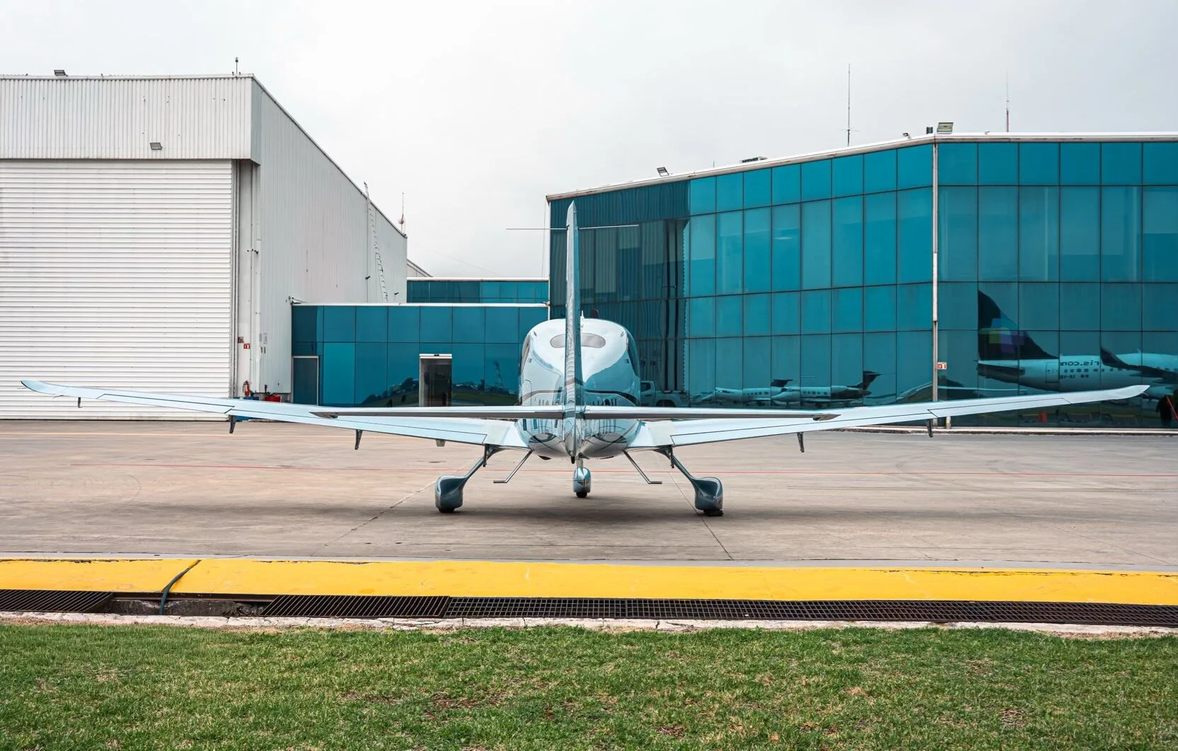 Rear view of a light blue Cirrus SR22T aircraft parked on an airfield in front of hangars.
