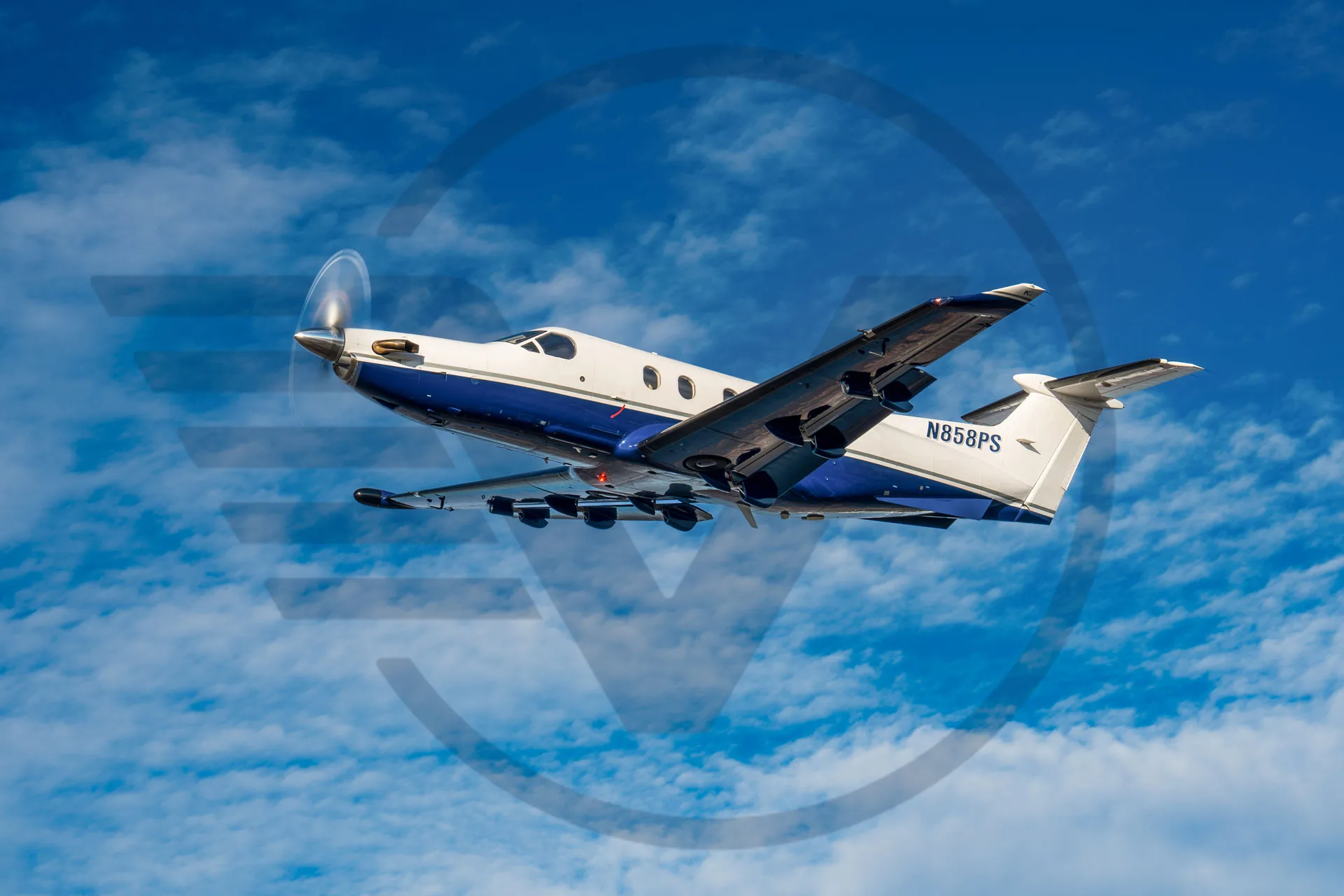 Pilatus PC-12 aircraft N858PS in flight against a blue sky with clouds.