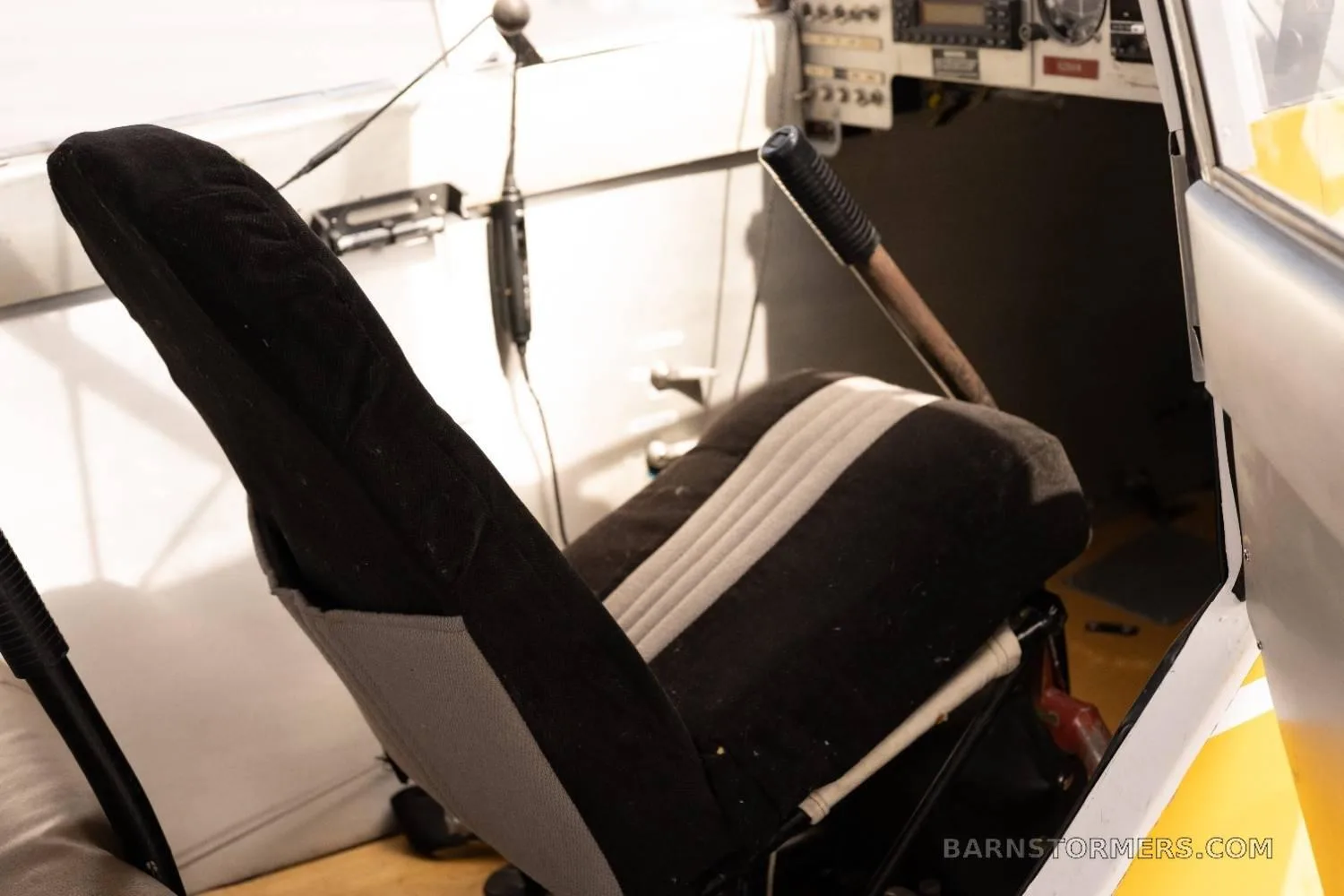 A black and white fabric aircraft seat with a partial view of the instrument panel and controls in the background.