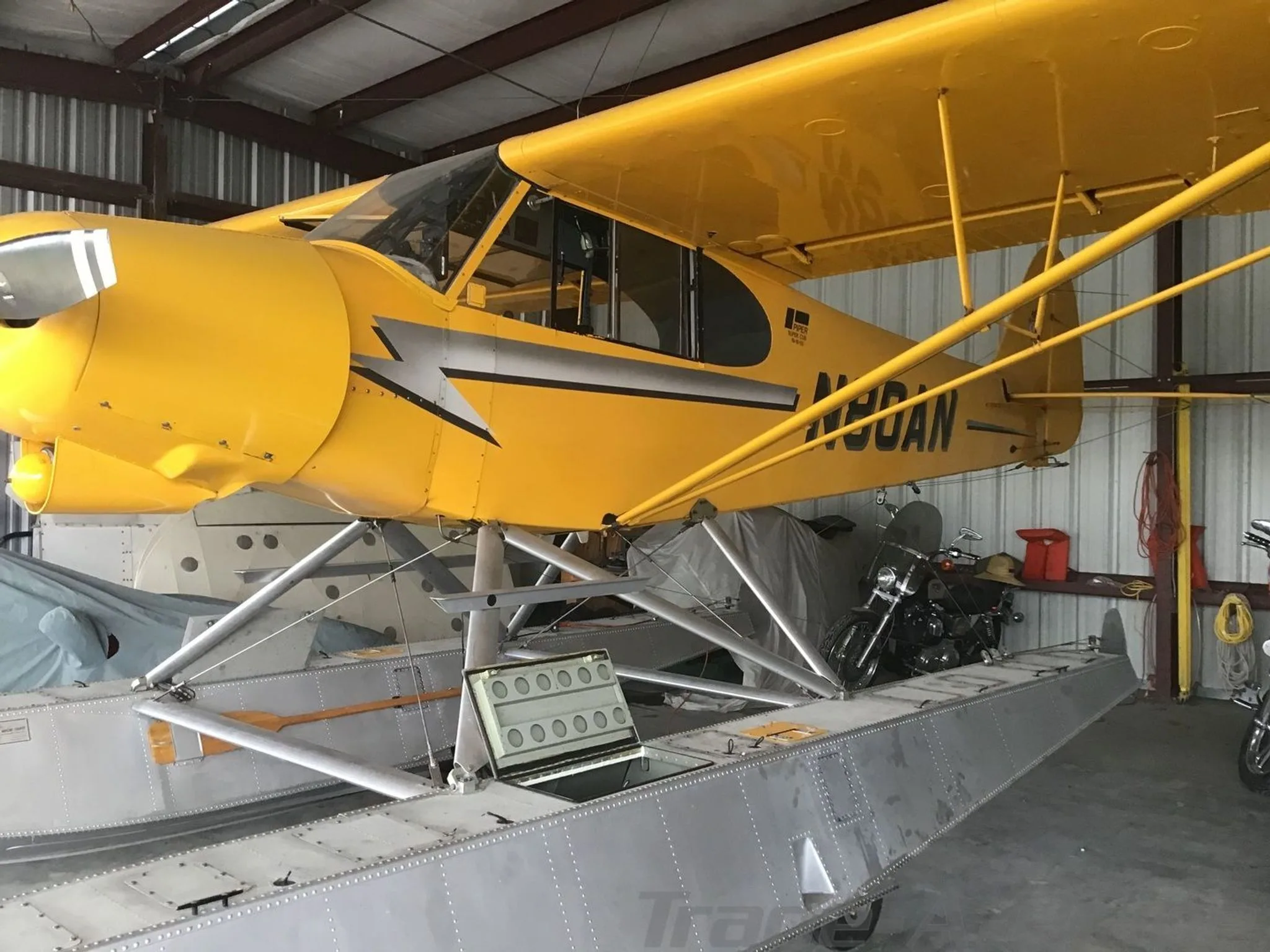 A yellow Piper Super Cub floatplane (N80AN) with silver floats parked inside a hangar.