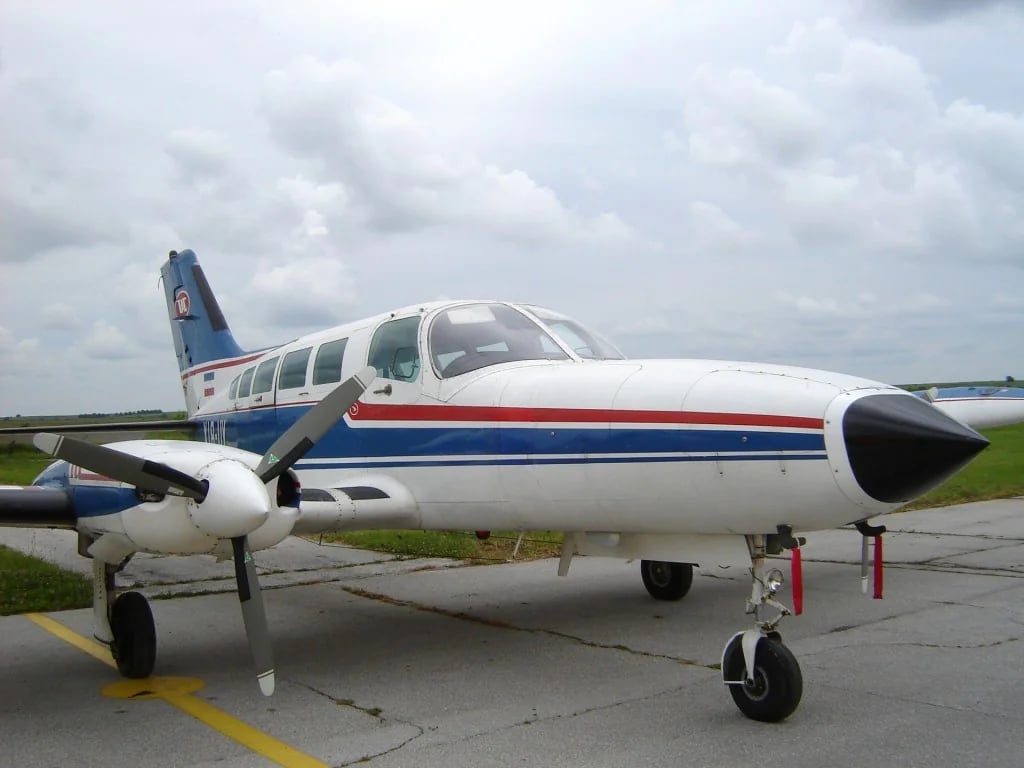 Front side view of a white and blue twin-engine aircraft on the tarmac.