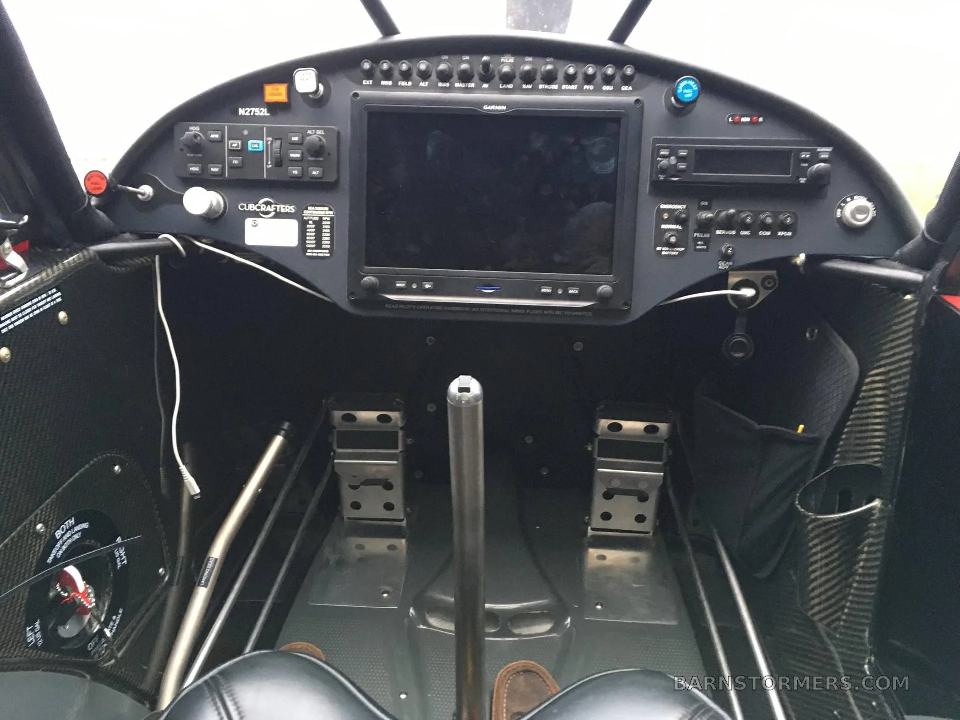 The cockpit of a CubCrafters aircraft, showing the instrument panel with a large Garmin display and rudder pedals.