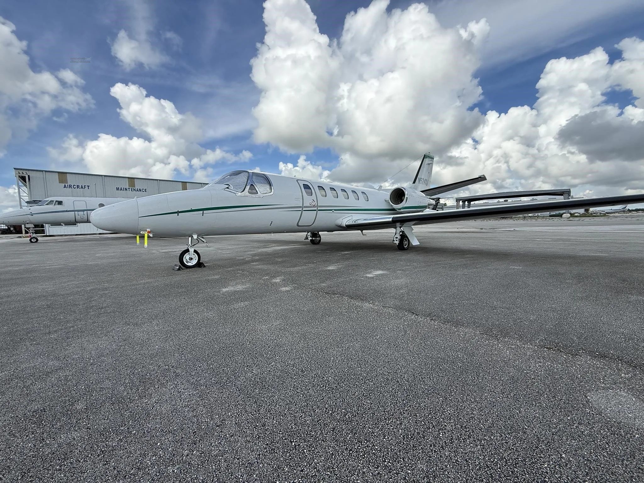 A white business jet with green stripes, registration N524XA, parked on an airport tarmac with a hangar in the background.