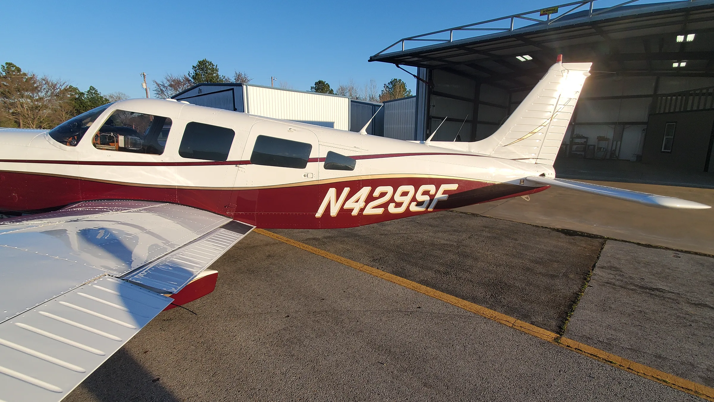 Side view of a white and maroon single-engine aircraft N429SF parked on an tarmac next to a hangar.