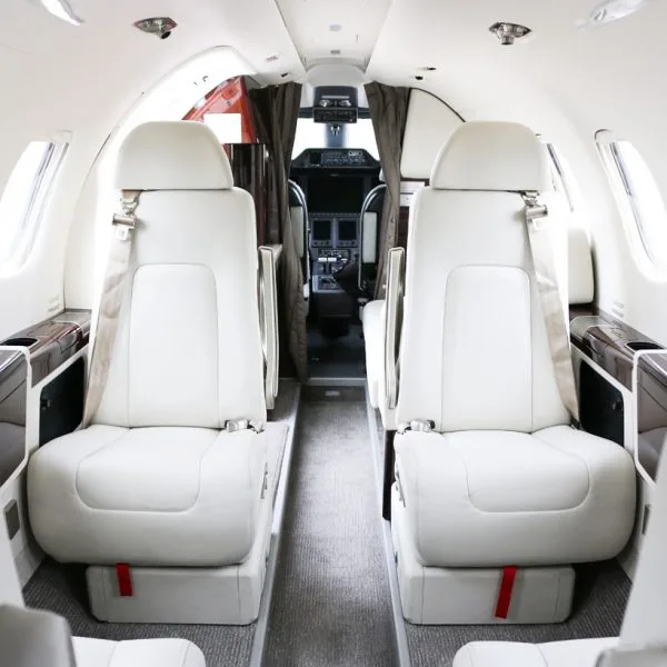 The interior cabin of a private jet with white leather seats and a view into the cockpit.
