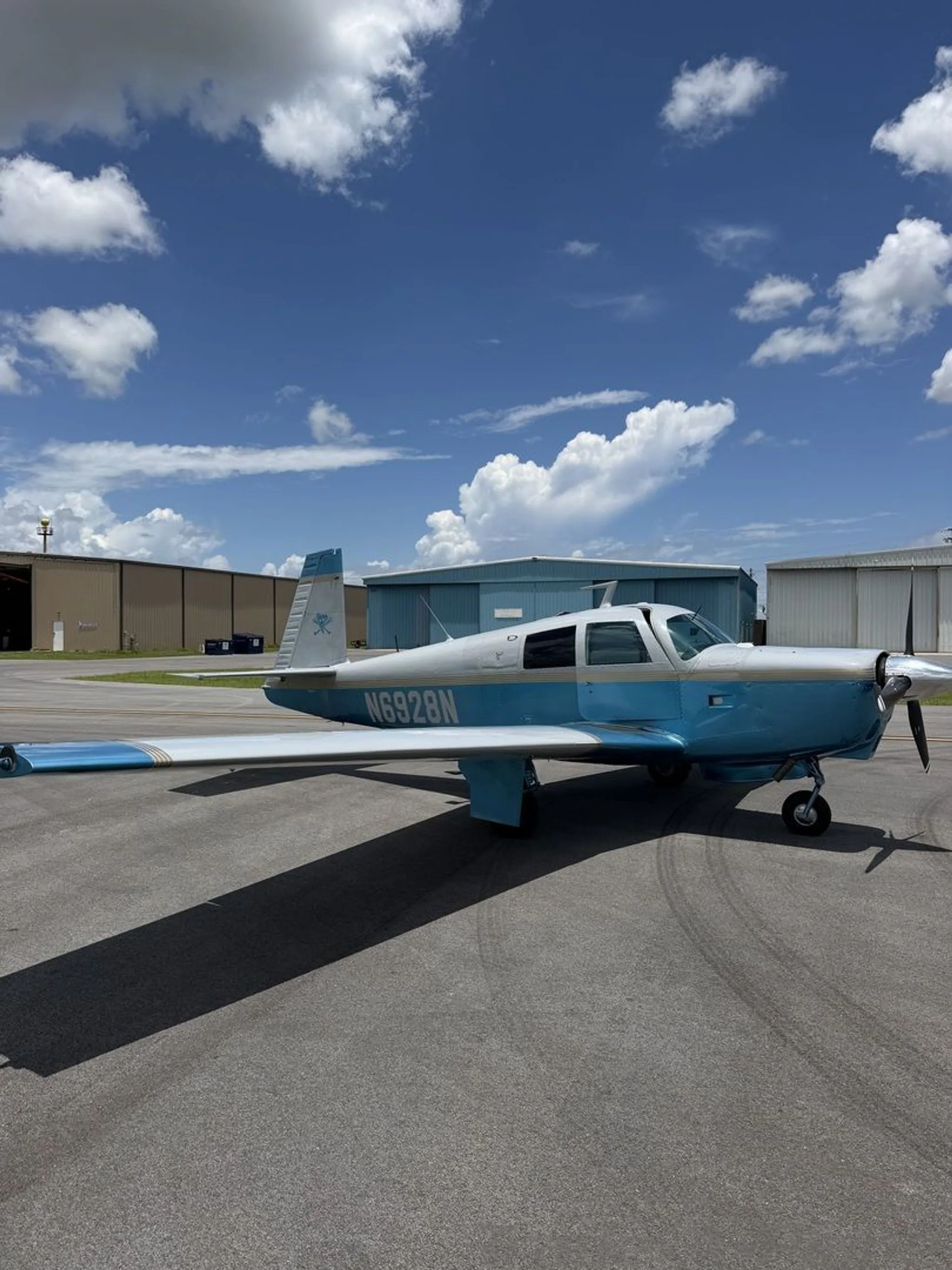A light blue and white single-engine aircraft, N6928N, parked on an airport tarmac under a partly cloudy sky.
