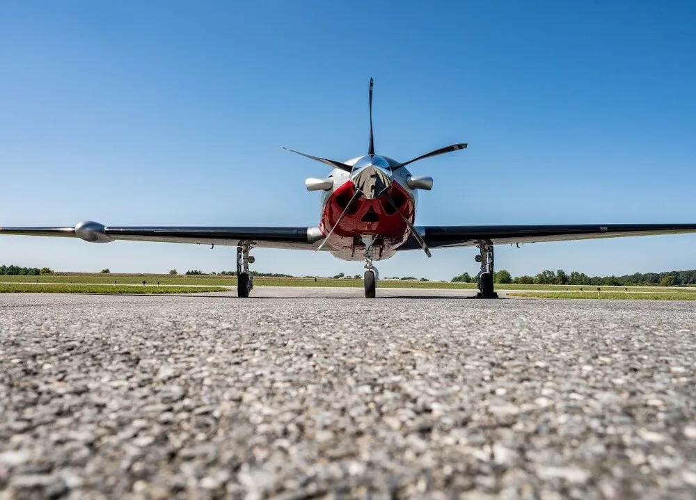 A low-angle front view of a Piper M600 aircraft with a red and silver paint scheme, parked on an airfield under a clear blue sky.