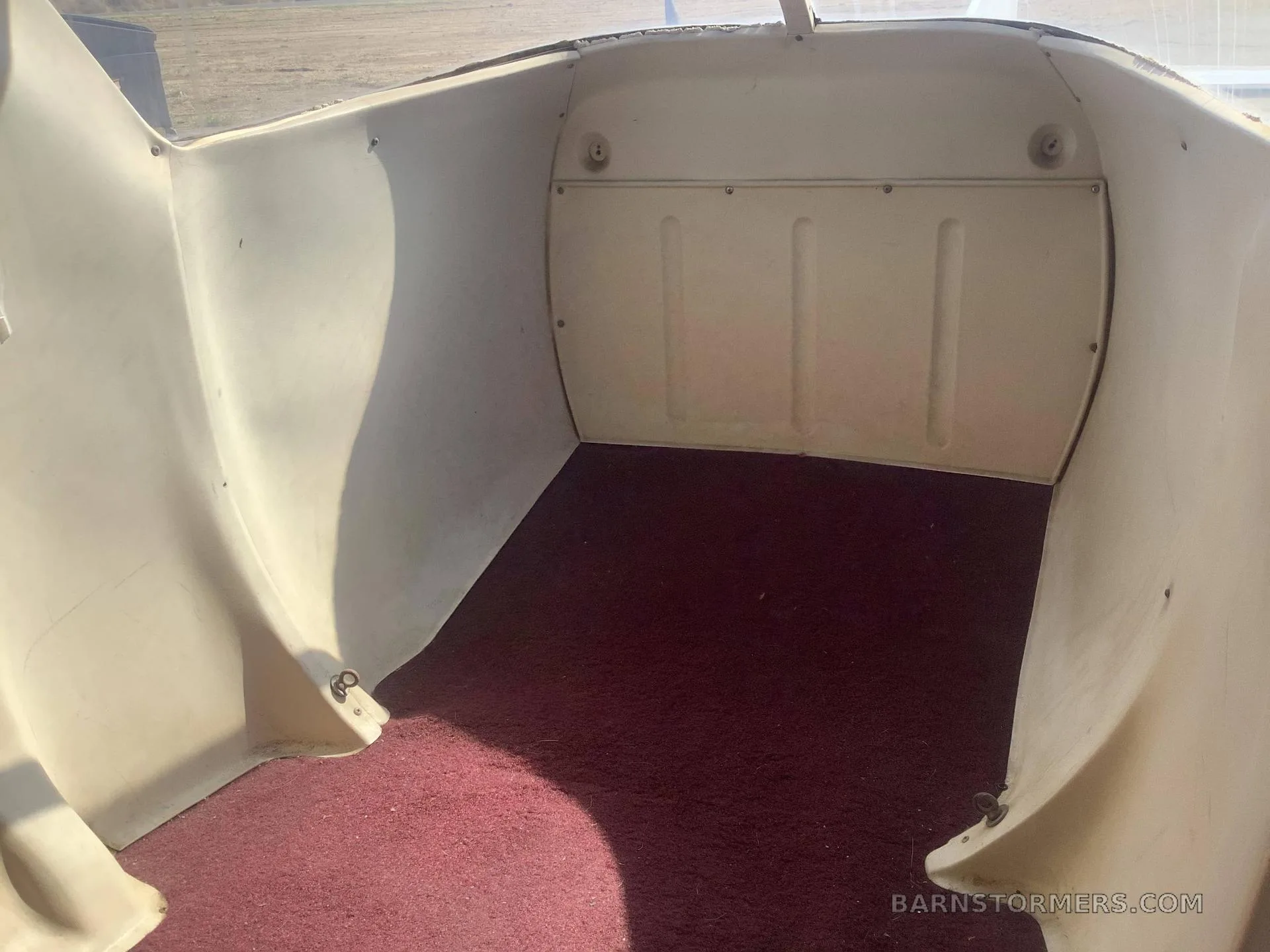 The empty baggage compartment of a small aircraft, featuring white walls and a red carpeted floor.