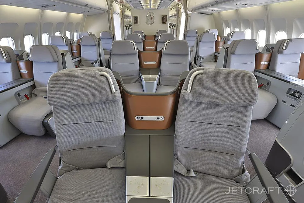 An interior view of an aircraft cabin featuring rows of grey premium economy or business class seats.