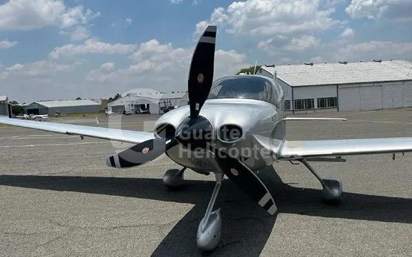 A front view of a silver Cirrus SR22 aircraft with a black propeller, parked on an airport tarmac.