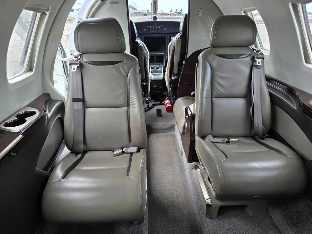 The interior cabin of a private jet, showing tan leather seats and a view into the cockpit.