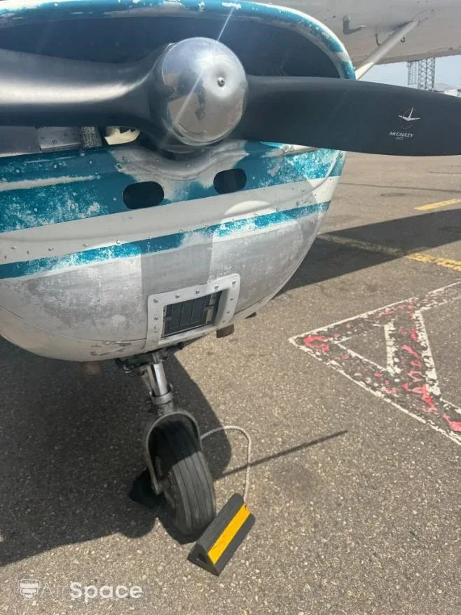 Close-up of the nose gear and propeller of a Cessna 150, with a yellow wheel chock.