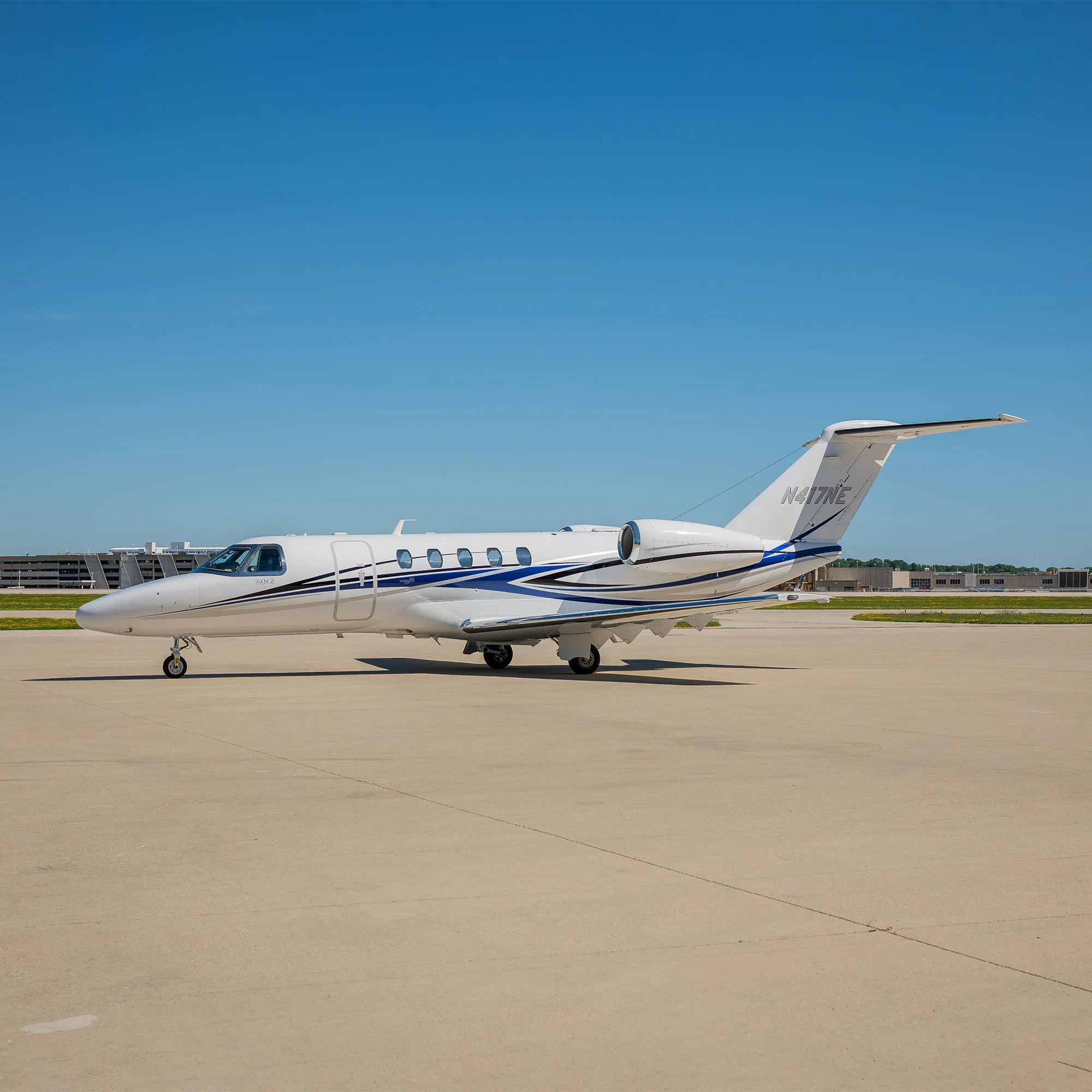 A white business jet with blue and grey stripes on an airfield under a clear blue sky.