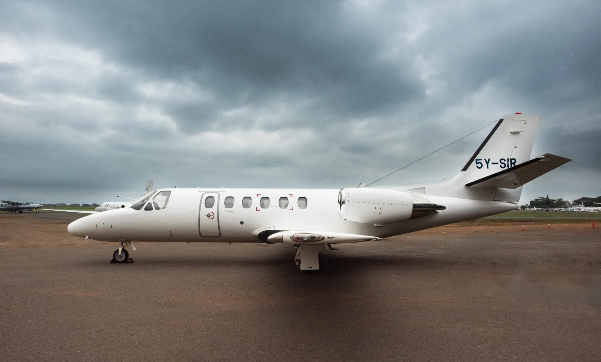 A white Cessna Citation business jet with registration 5Y-SIR parked on a tarmac under a cloudy sky.