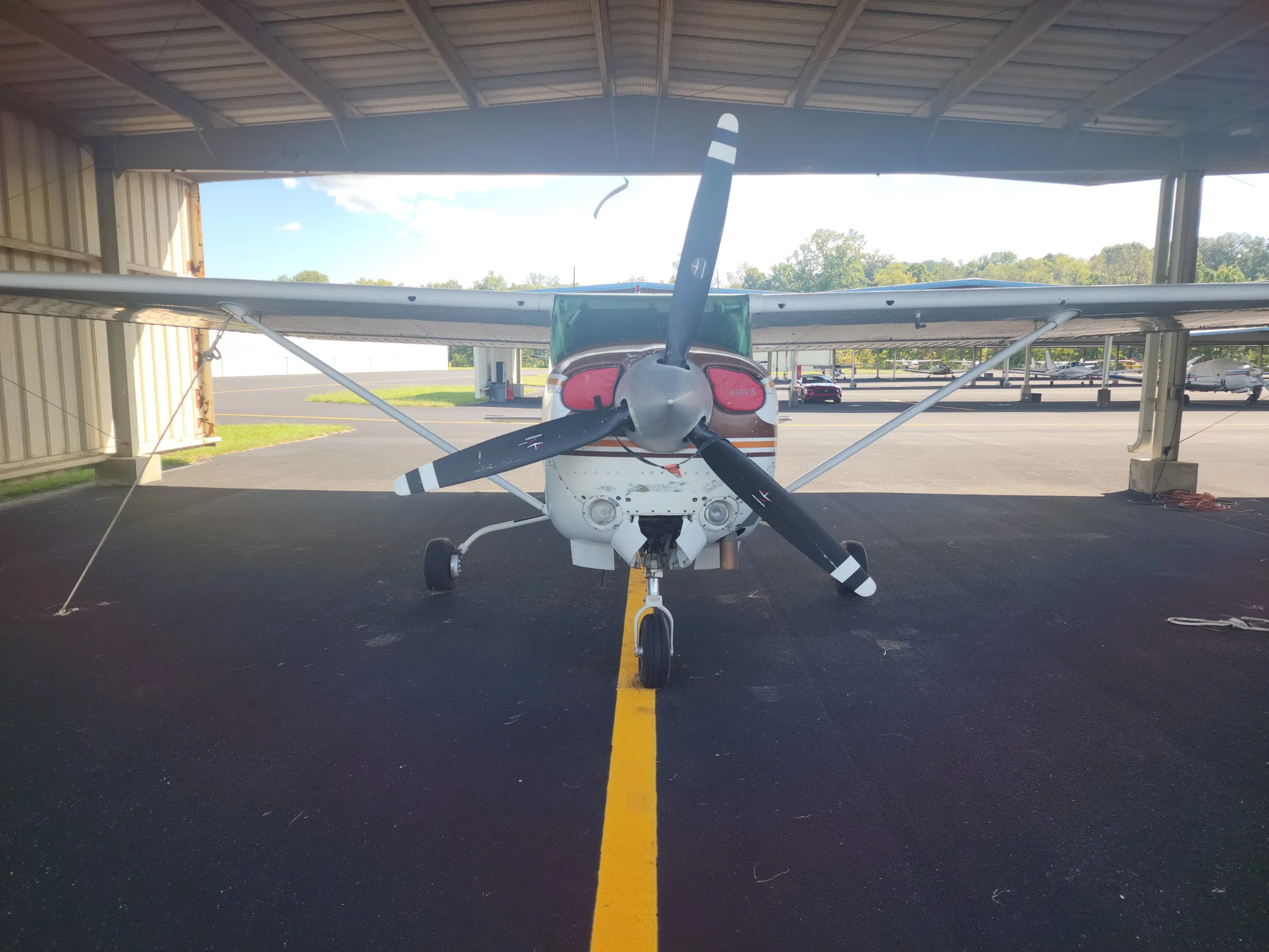 Front view of a white and brown Cessna Skylane RG II (N5019S) with a three-bladed propeller, parked in a hangar.