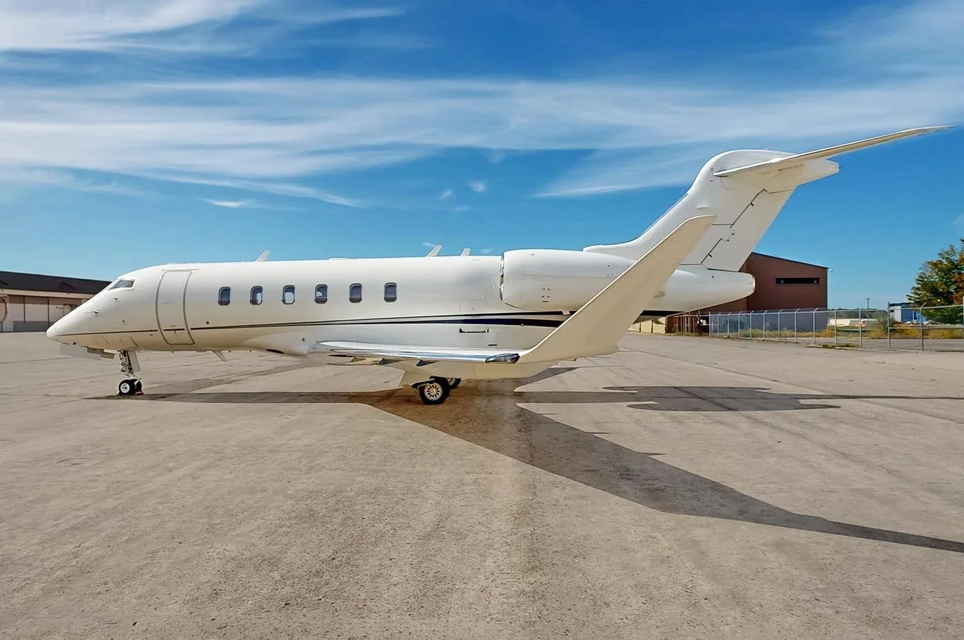 A white Bombardier Challenger business jet parked on an asphalt tarmac under a blue sky.