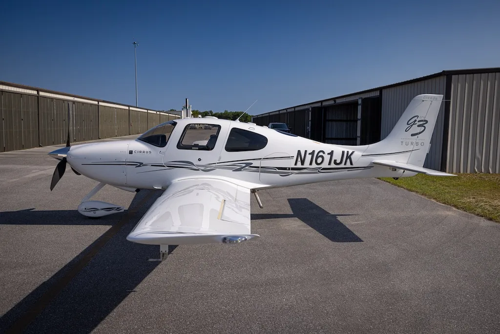 A white Cirrus SR22 G3 Turbo aircraft, registration N161JK, parked on an asphalt tarmac with hangars in the background.