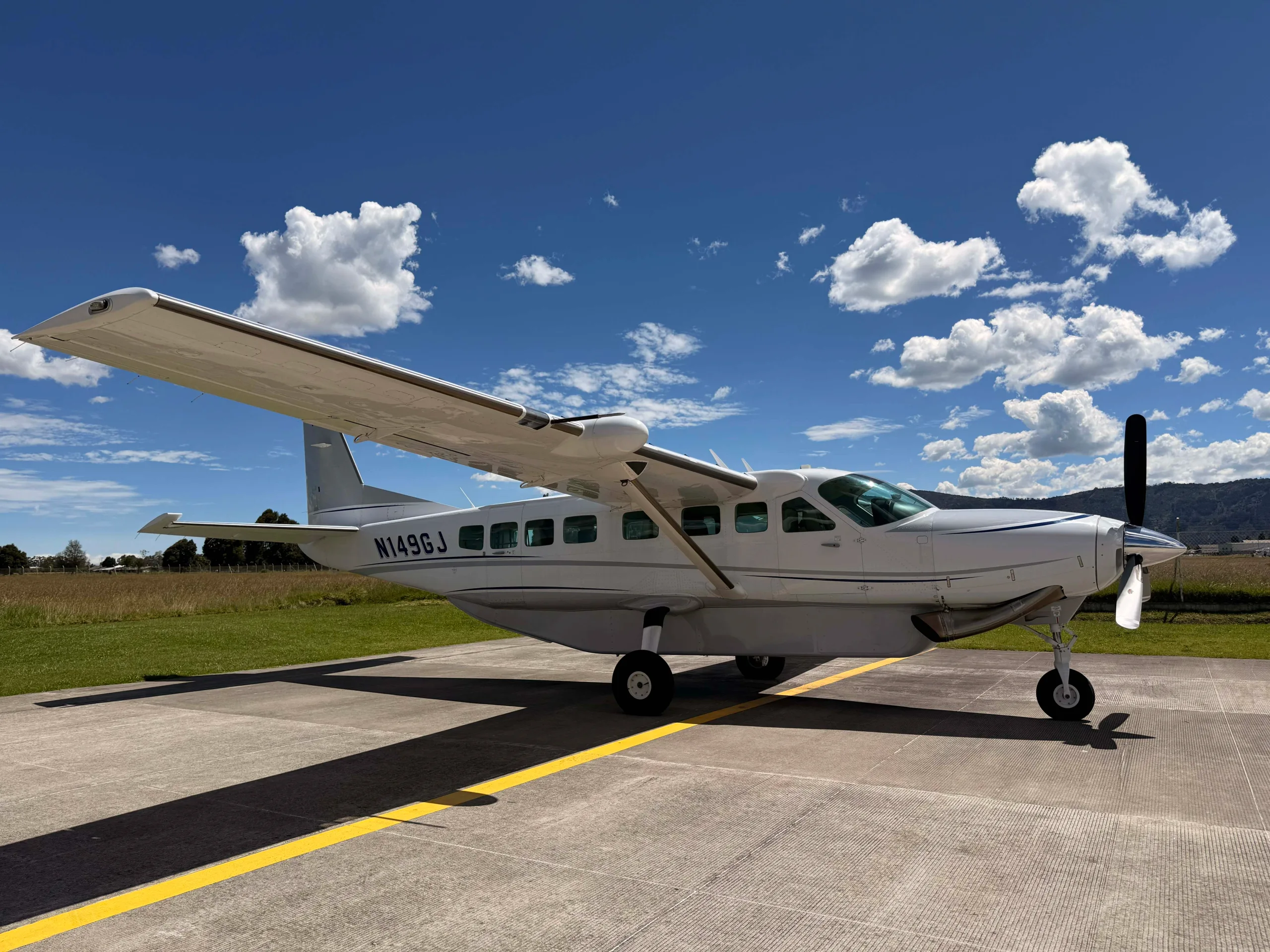 A white Cessna Caravan N149GJ parked on an airfield with a blue sky and clouds.