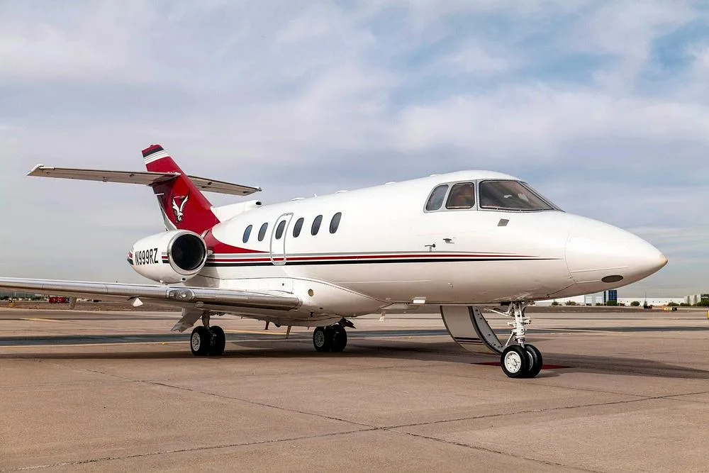 A side view of the N999RZ business jet, painted white with red and black stripes, parked on an airfield.