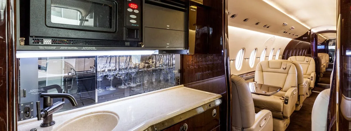 A well-appointed aircraft galley with a microwave, sink, and a rack of glassware, looking into the cabin.