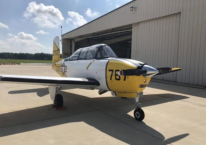 A white and yellow T-34 Mentor aircraft with "USAF" markings and "767" on the nose, parked in front of a hangar.