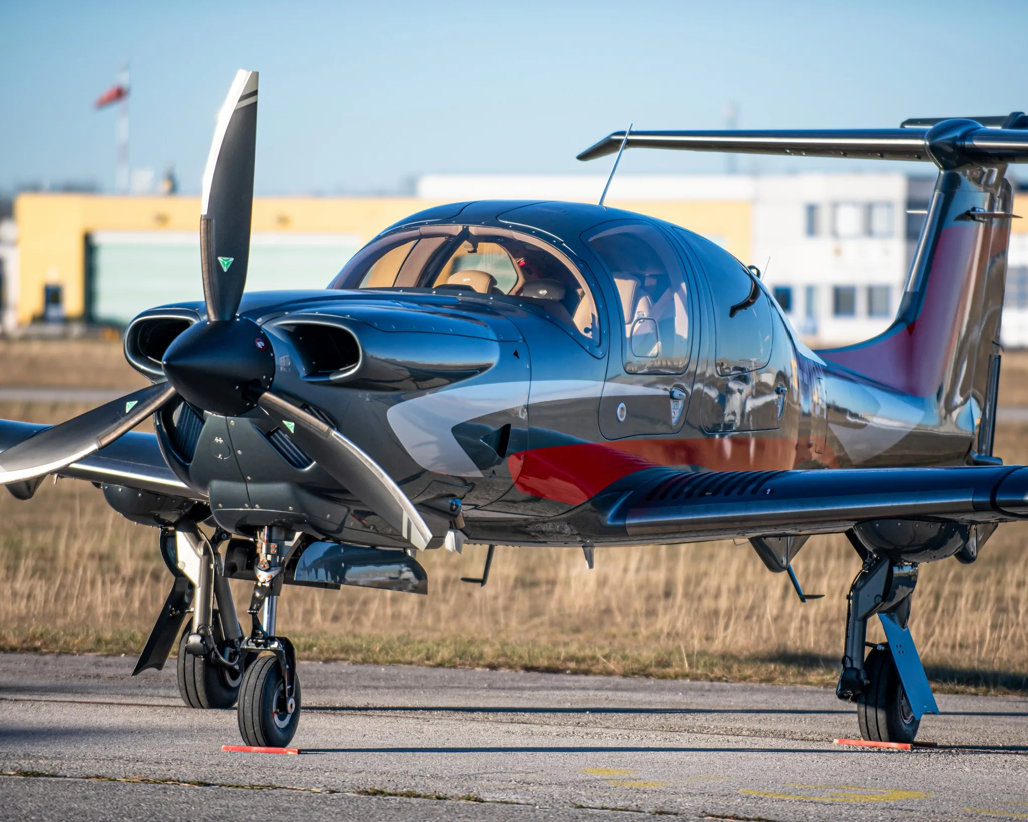 A dark grey single-engine propeller aircraft with red and white accents on an airfield, viewed from the front-left.