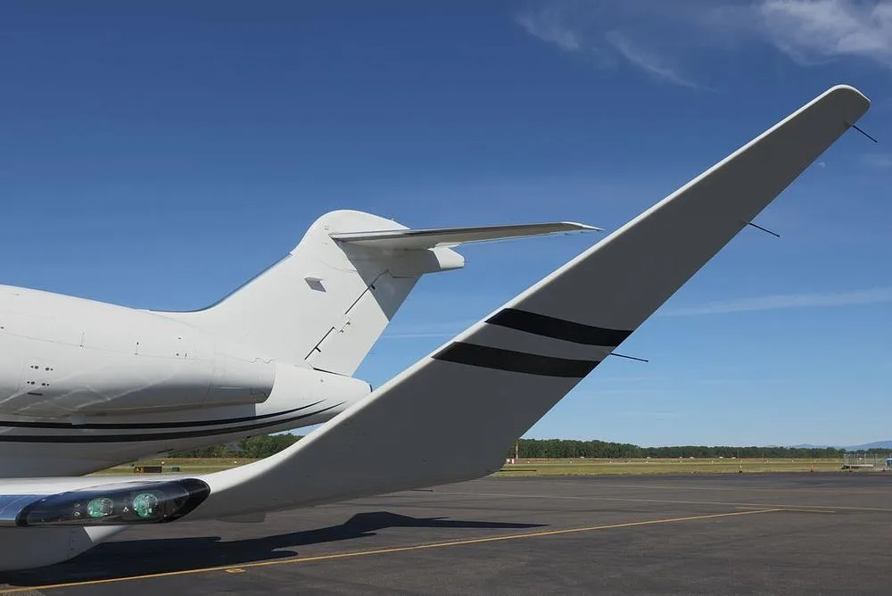 A close-up view of the white tail and winglet with black stripes of a business jet, parked on an asphalt tarmac.