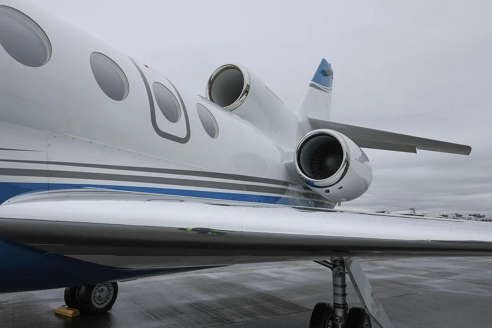 A close-up view of the engines, wing, and fuselage of a white and blue Dassault Falcon 900EX business jet.