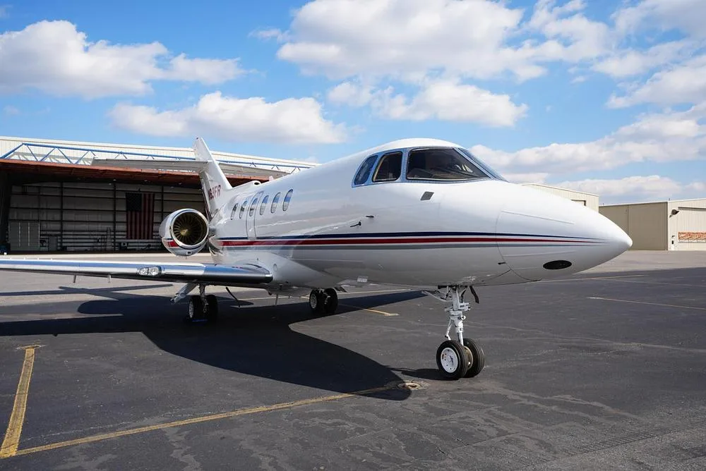 A front-left view of the white business jet N69FR parked on an asphalt tarmac in front of a hangar.